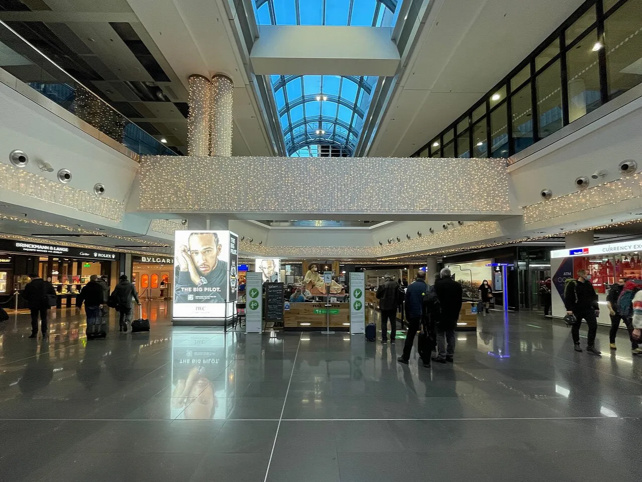 Menschen in einer hellen mehrgeschossigen Flughafenhalle mit geschwungenen Galerien in Frankfurt.