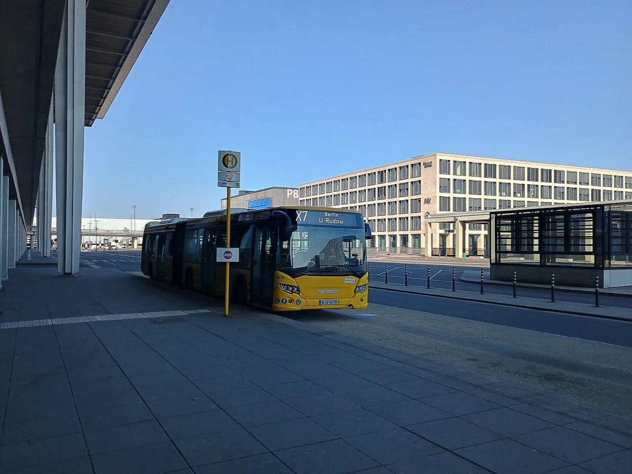 Ein gelber Linienbus an der überdachten Haltestelle vor Terminal 1 des Flughafens BER.